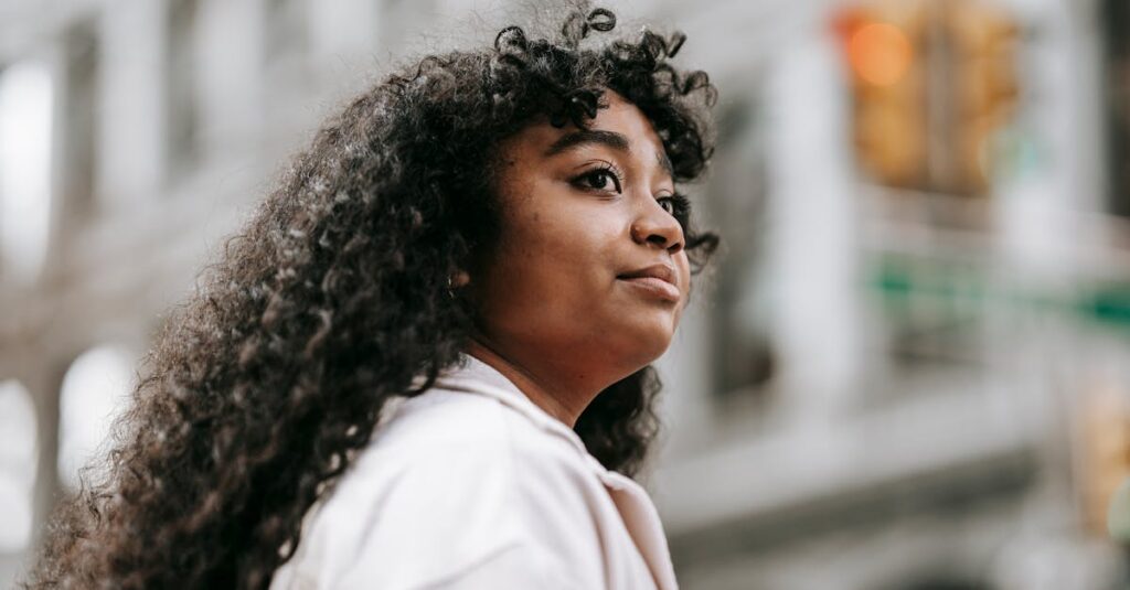 Portrait of a young woman with curly hair standing in a city, exuding confidence and independence.