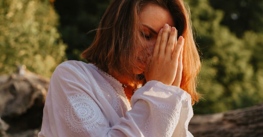 Woman meditating outdoors, eyes closed in peaceful prayer pose.