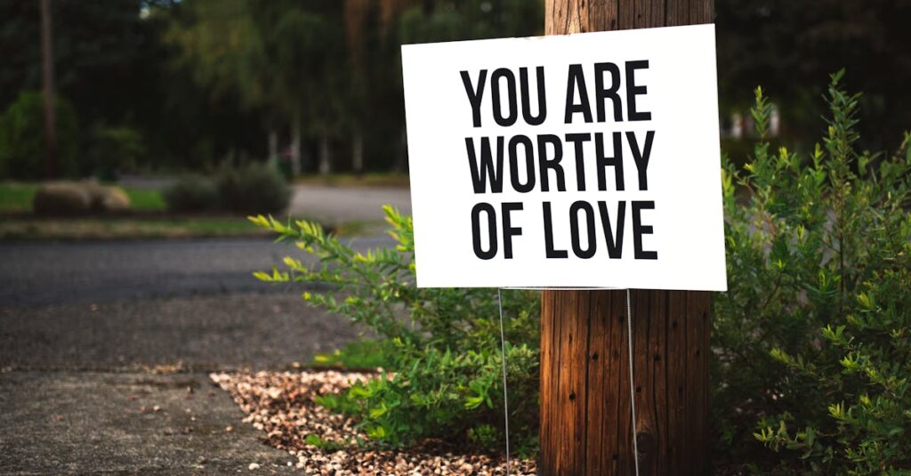 A positive message sign "You are worthy of love" in a park setting.