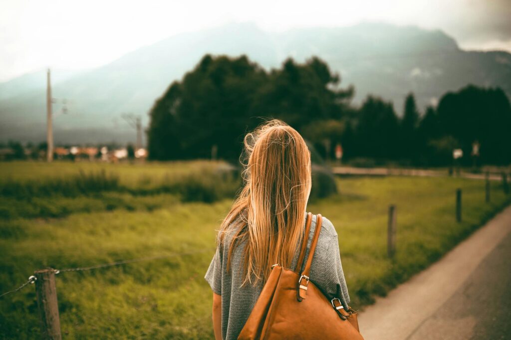 A woman with blonde hair and a backpack explores a scenic mountain landscape at sunset, capturing a sense of freedom and travel.