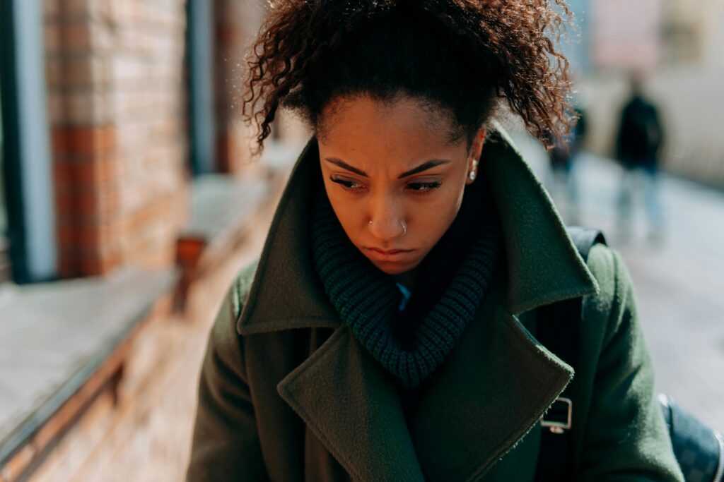 A young woman in a trench coat appears thoughtful and pensive walking down a city street.