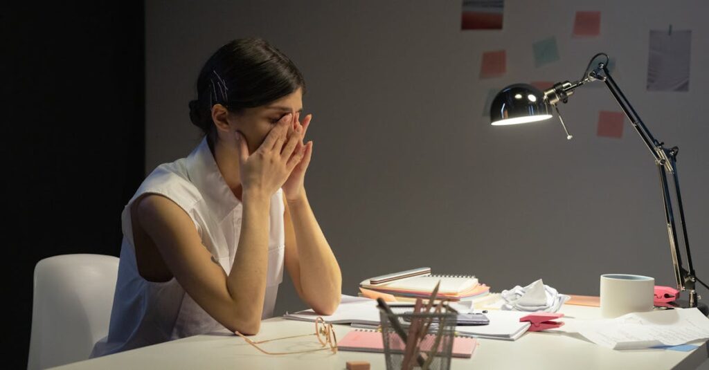 A stressed businesswoman rubs her eyes at a cluttered desk, overwhelmed by work.