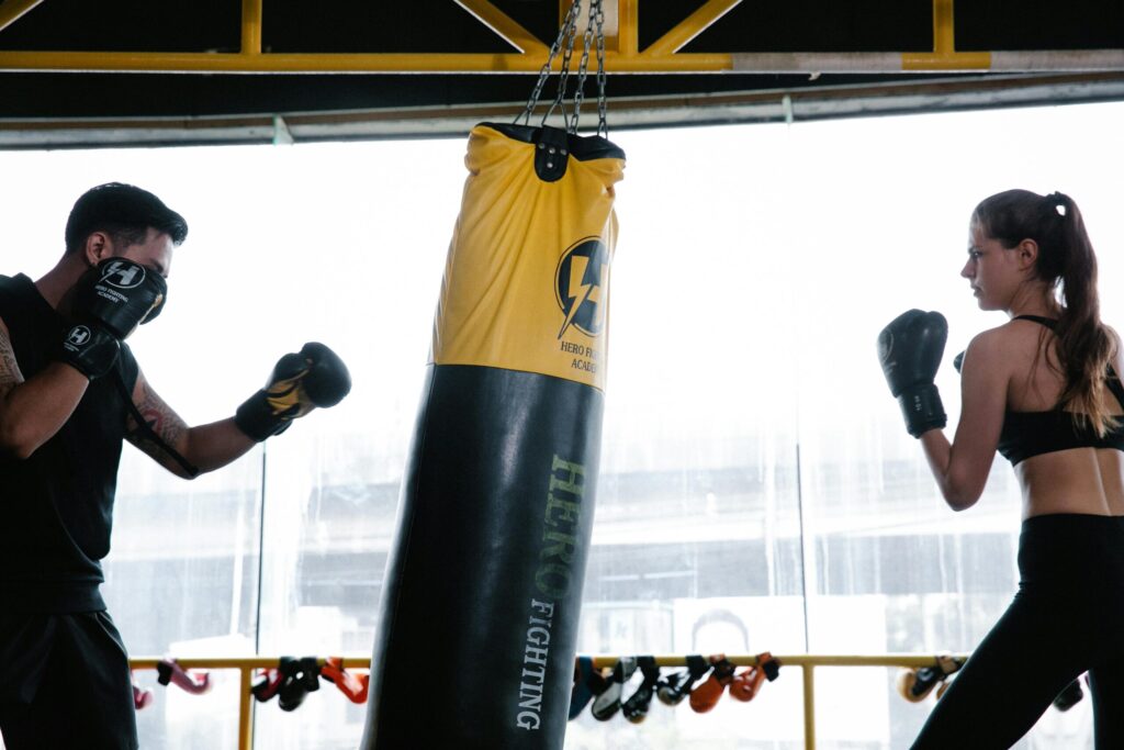 Two people engage in boxing training with a punching bag indoors, focusing on technique and strength.