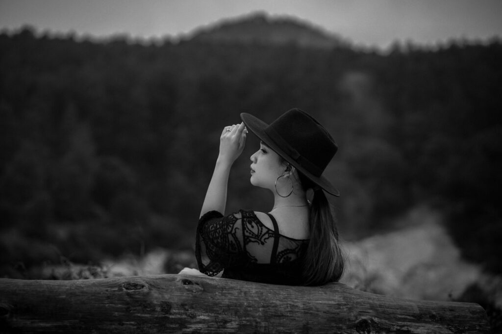 Graceful profile of a woman in a lace dress and black hat, captured in a tranquil forest setting.