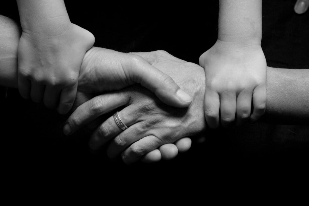 Monochrome image of a child's and adult's hands clasped together symbolizing trust and connection.
