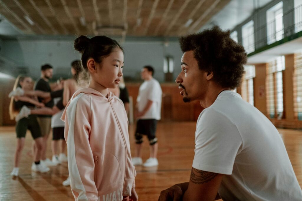 Coach and young girl engage in focused conversation during gym training session.
