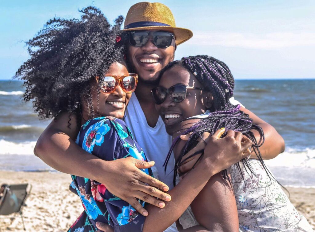 Three friends enjoying a sunny day at the beach, embracing with smiles.