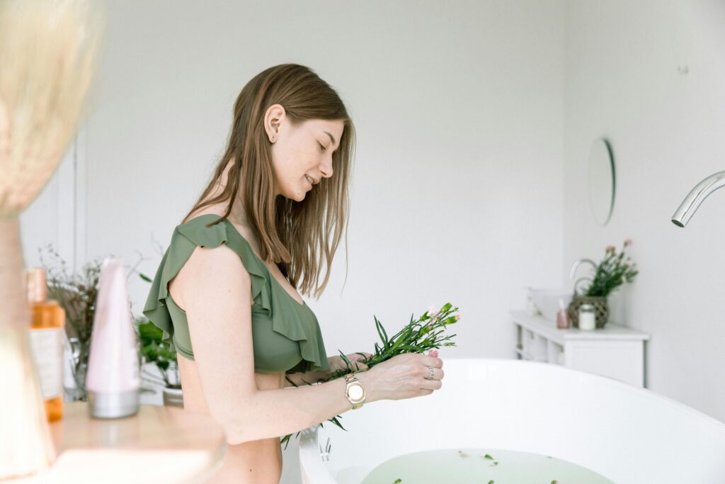 A woman in a bikini arranging flowers in a bathtub for a spa-like atmosphere indoors.
