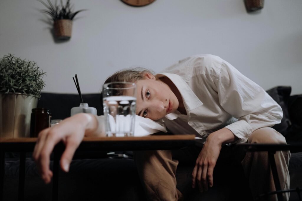 Young woman in white shirt, head resting on table, overwhelmed and fatigued at home.