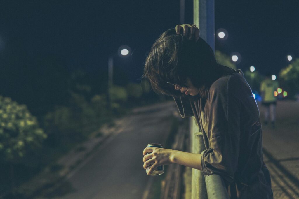 Person standing alone at night, leaning with a drink, capturing a contemplative mood.