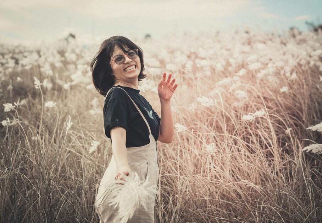 A smiling woman in a black shirt enjoys the outdoors in a wheat field.