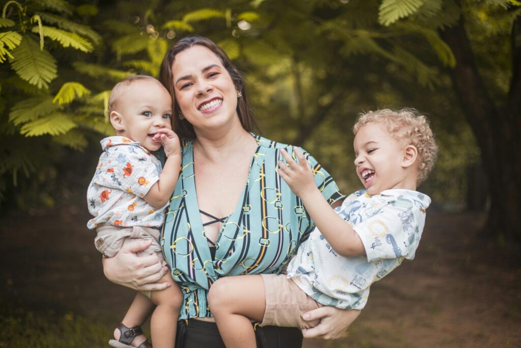 A joyful mother embraces her two sons in a lush park setting, capturing a sweet family moment.