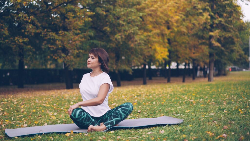 Woman practicing yoga in a park during autumn, surrounded by colorful leaves.