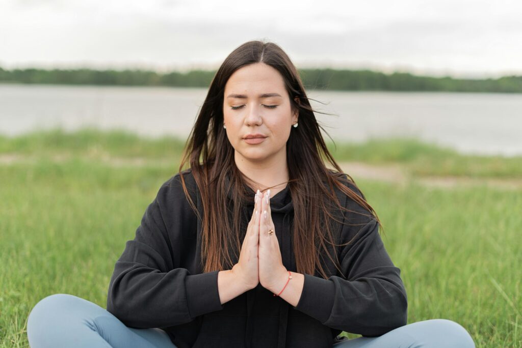 A serene woman practicing meditation outdoors near a lake, promoting wellness and relaxation.